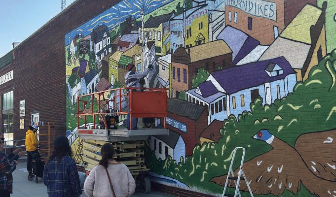 Mural designer Ryan Cramer and his daughter, Irmina, look on as Impact Art’s Derek Rusher and Josh Arias put the finishing touches on a new mural downtown Cambridge.