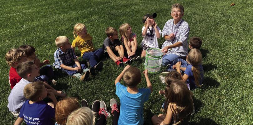 Betsy Hoxmeier sits outside with her 2022-2023 kindergarten class to release monarch butterflies as part of their lesson.